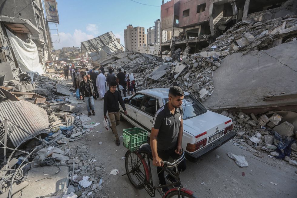 Photograph of a row of Palestinians walking past the remains of buildings destroyed by Israeli airstrikes on Khan Younis.