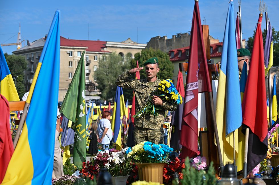 Photograph of a serviceman, surrounded by flags, saluting during the commemoration of Ukrainian defenders who died in the war.