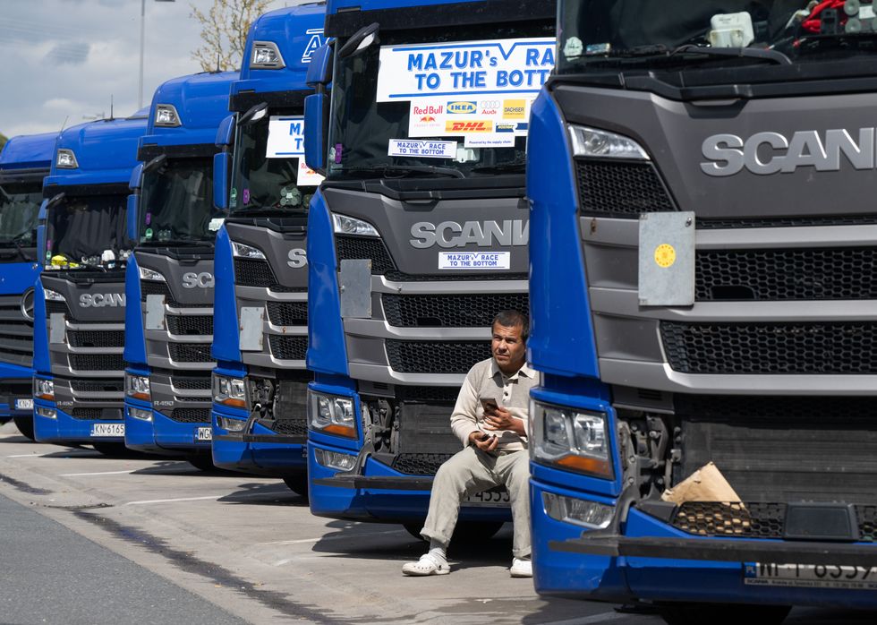 Photograph of a trucker sitting on the grille of a blue truck.
