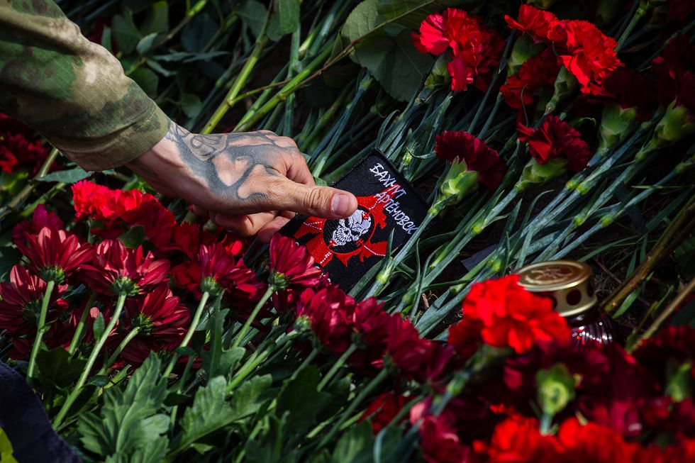 Photograph of a Wagner member laying his patch on flowers which are honouring the memory of Yevgeny Prigozhin.