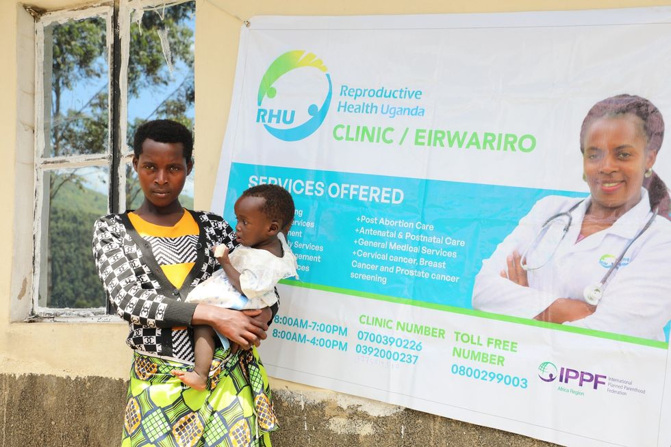 Photograph of a woman and her baby in front of ​Reproductive Health Uganda poster