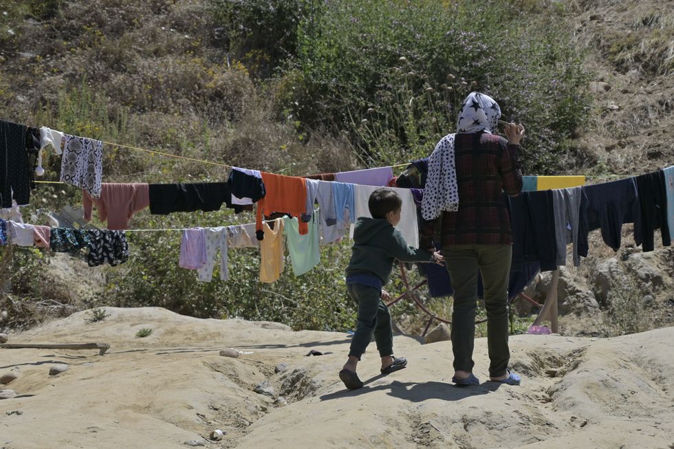Photograph of a woman and young child hanging clothing, as they wait for appointments at the Center on Global Justice being built at one of Tijuana's largest operational shelters​.