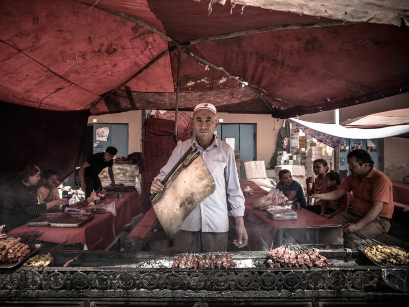 Photograph of an ethnic Uyghur man cooking Kebab in Kashgar bazaar.​