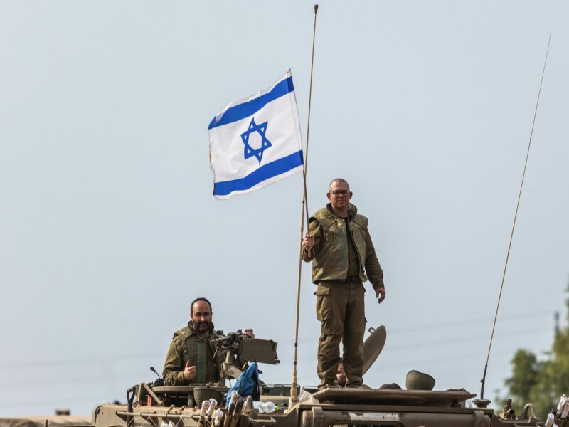 Photograph of an Israeli soldier holding an Israeli flag on top of a tank.