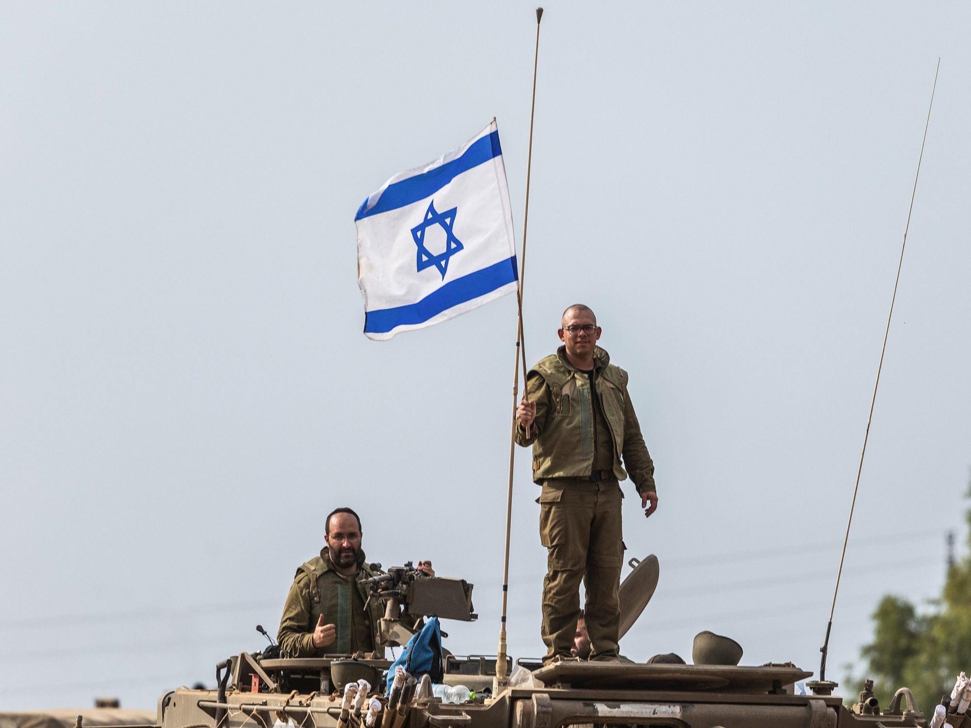 Photograph of an Israeli soldier holding an Israeli flag on top of a tank.