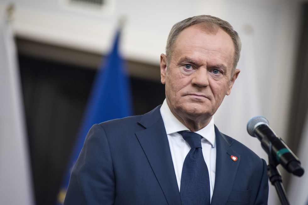 Photograph of Donald Tusk frowning in front of a microphone