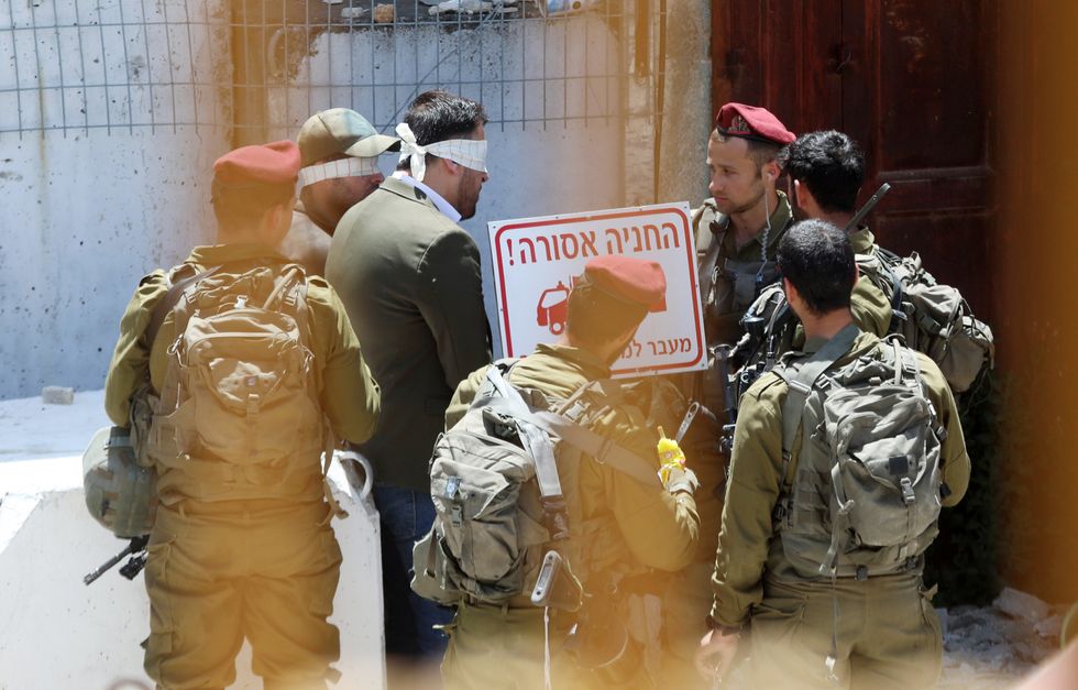 Photograph of IDF soldiers arresting two Palestinian men and bandaging their eyes.