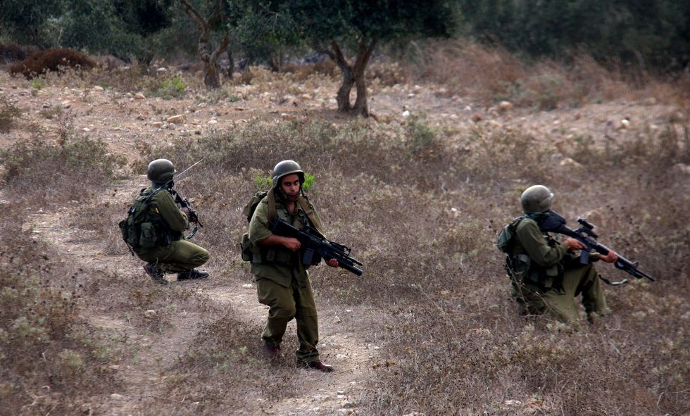 Photograph of IDF soldiers patrolling an olive grove with rifles in hand.