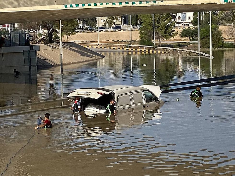 Photograph of Libyan Red Crescent members submerged in flood water as they attempt to open the roads that have been engulfed.