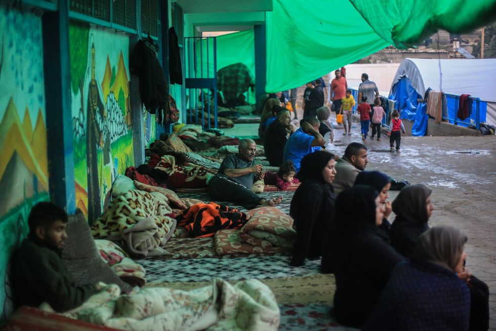 Photograph of Palestinians seen at an UNRWA camp in Khan Younis, southern Gaza.​ Women and men sit on cots used as beds.