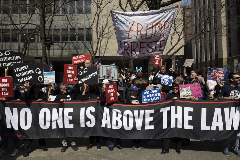 Photograph of people holding up a banner that reads "No One Is Above The Law" and chant outside Manhattan Criminal Court