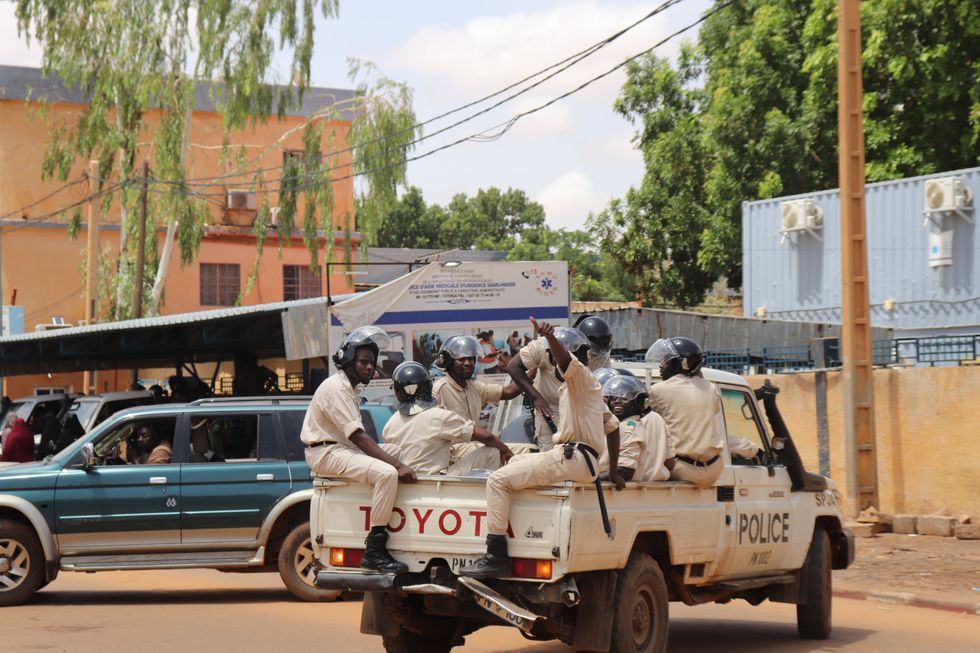 Photograph of police officers on the sidelines of a march in support of the coup plotters in Niamey, Niger. They sit on the back of a pickup truck.