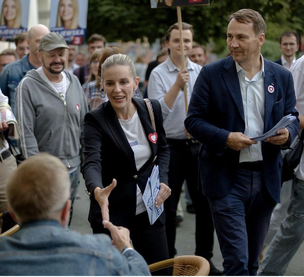Photograph of Polish candidate Aleksandra Gajewska on a leaflet walk. She is extending her hand to shake that of a man sitting down.