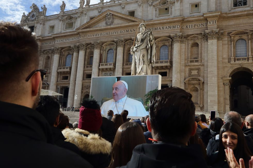Photograph of Pope Francis speaking on a large screen in front of a church.
