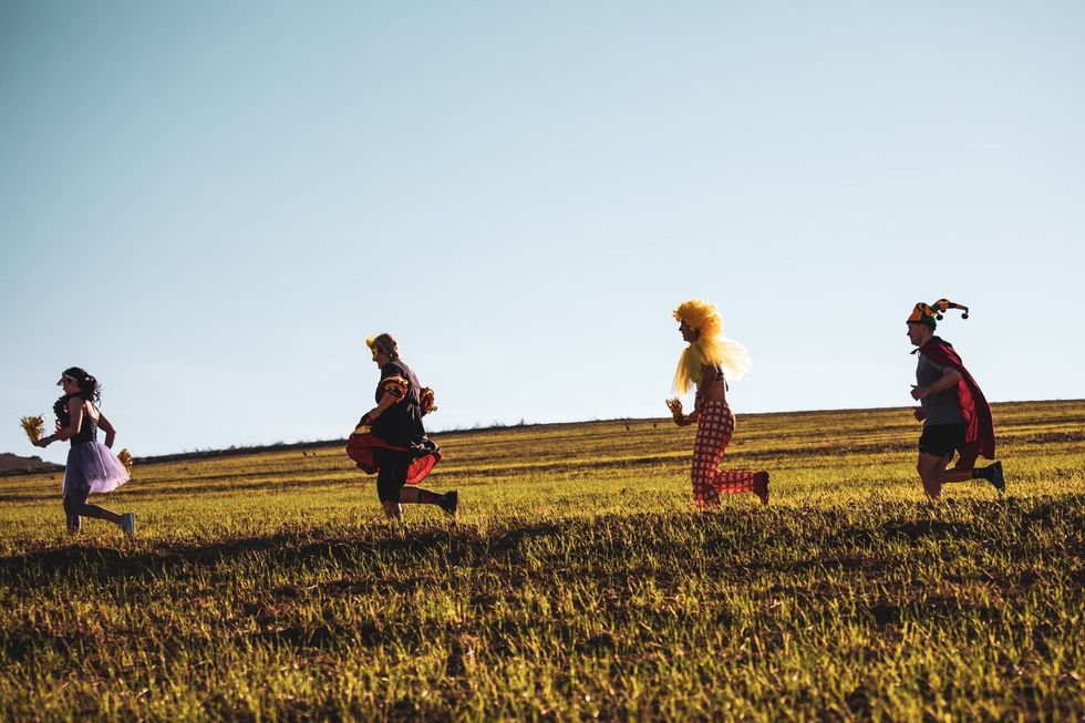 Photograph of runners dressed up in carnival costumes during the Cape Wine Marathon​. They are down a hill, one at a time.