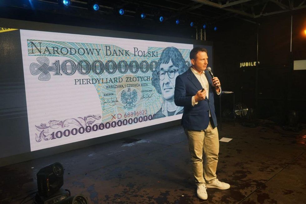 photograph of Sławomir Mentzen on stage in front of supporters. Behind him a projection shows a polish banknote with an imaginary trillion dollar value.
