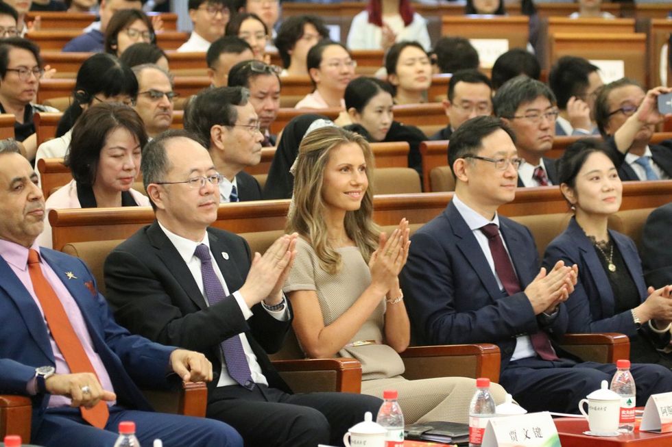 Photograph of Syrian First Lady Asma al-Assad sitting in a university room, and clapping towards the stage.