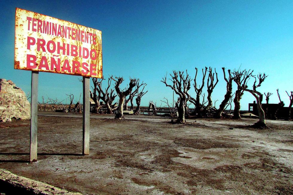 Photograph of the ​ruins of Villa Epecuén, with a sign that reads 'swimming is prohibited'.