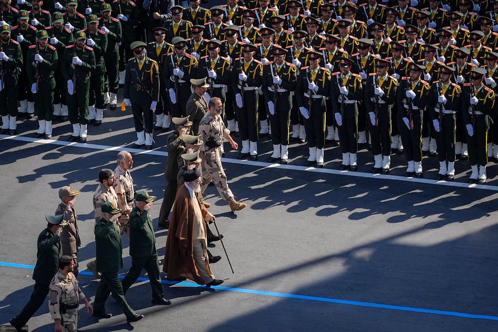 Photograph of the Iranian supreme leader walking with generals as they review rows of armed forces cadets during their graduation ceremony.