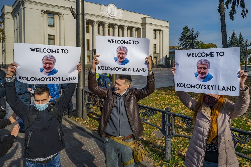 Photograph of three protestors holding up signs with a photograph of oligarch Ihor Kolomoisky which read "Welcome to Kolomoyski land"