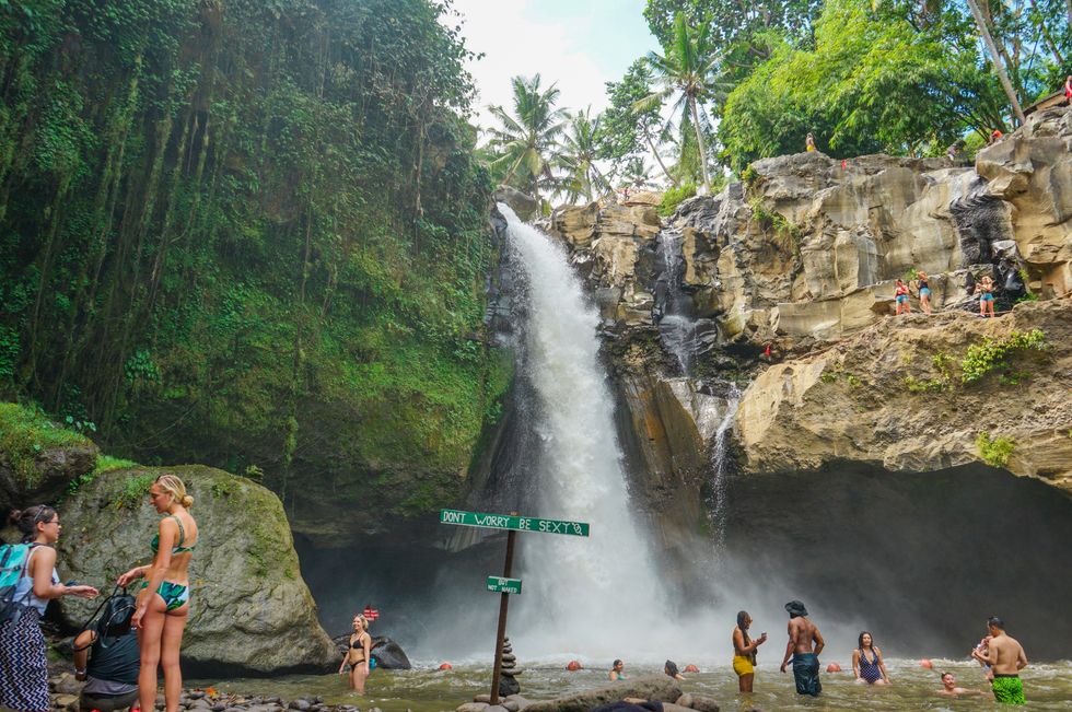 Photograph of toruists at the "Don't Worry be sexy but not naked" sign in Tegenungan Waterfall, Bali, Indonesia.
