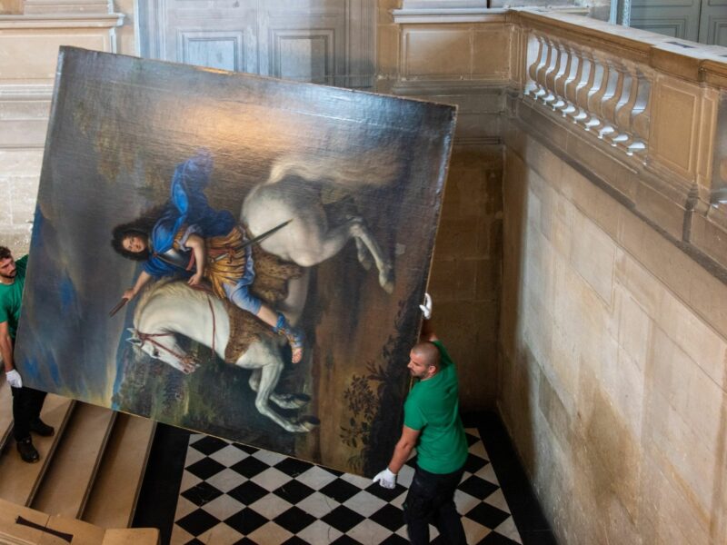 Photograph of two workers moving a painting inside the Palace of Versailles​