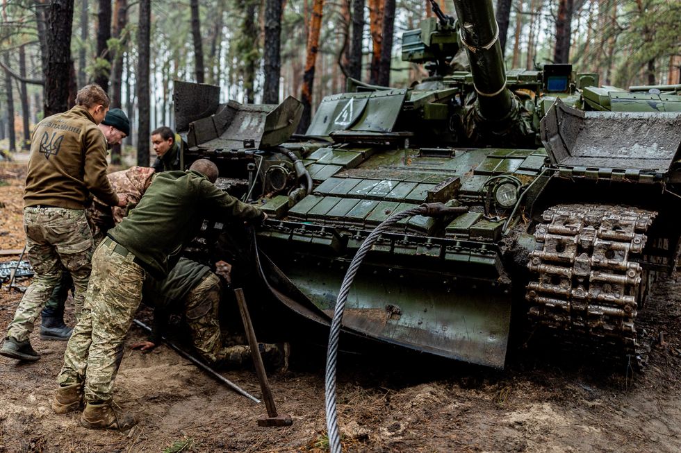 Photograph of Ukranian soldiers checking their tank after an action in the forest.