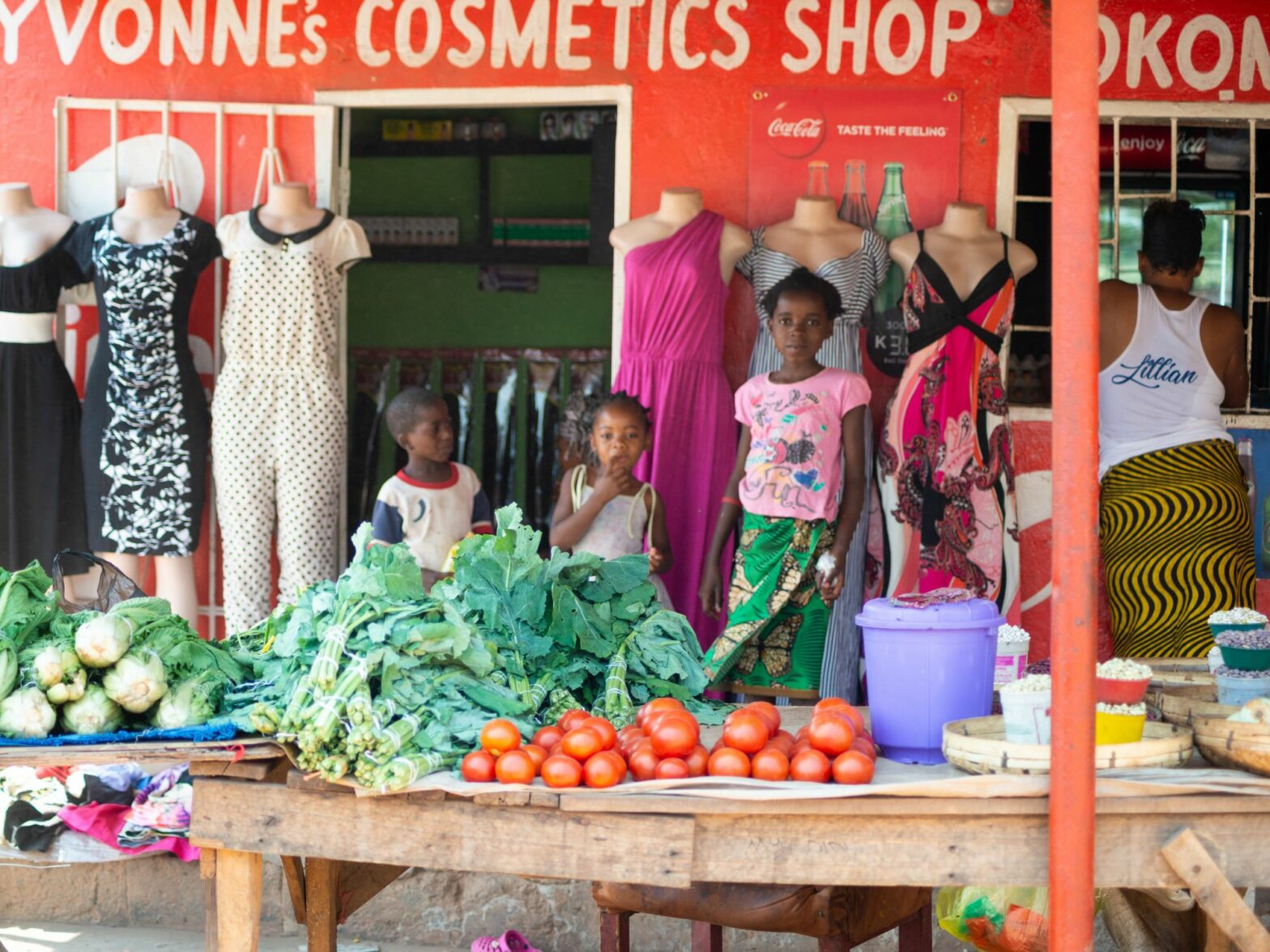 Photograph of young girls in Zambia standing behind a vegetable stand.