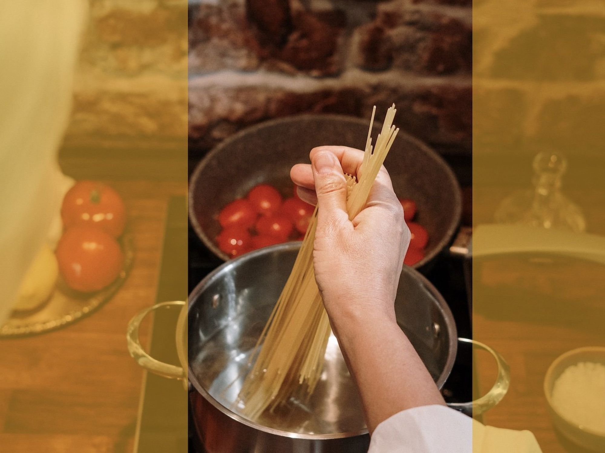 Photograph taken from overhead of a woman dropping spaghetti into boiling water. Behind her hand one can see tomatoes cooking in a pan.