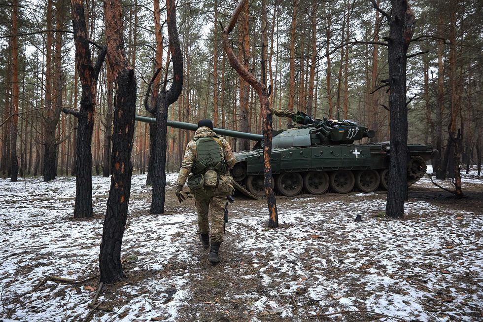 Picture of a Ukrainian soldier walking towards a heavy tank in a snowy forest.