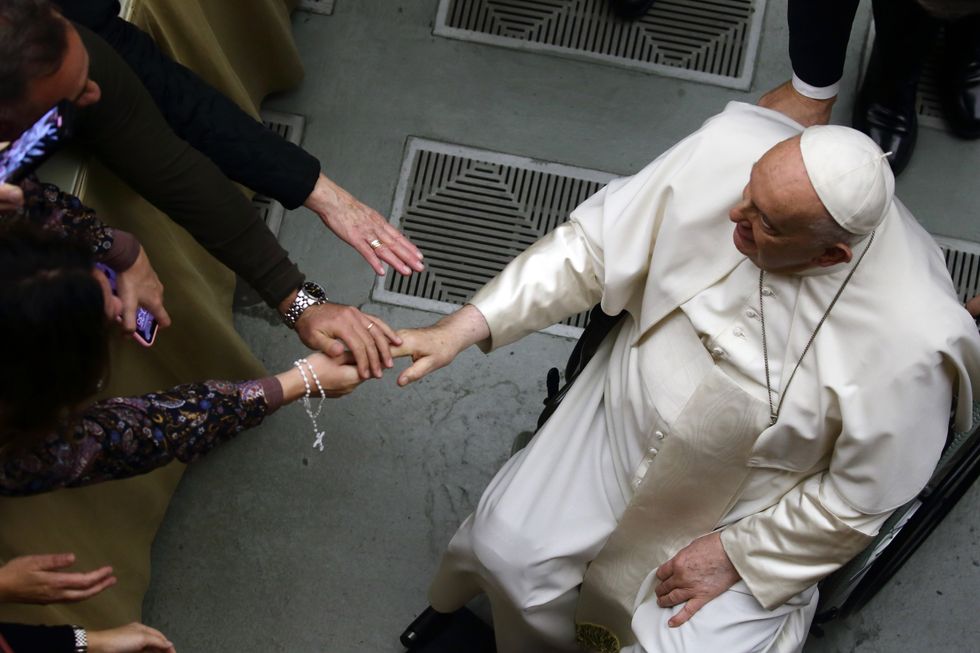 Pope Francis reaches over to tough the hands of devotees during his General Audience at the Vatican.​
