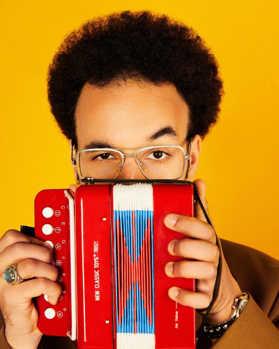 Portrait of Theo Ould hiding his face behind a miniature accordion