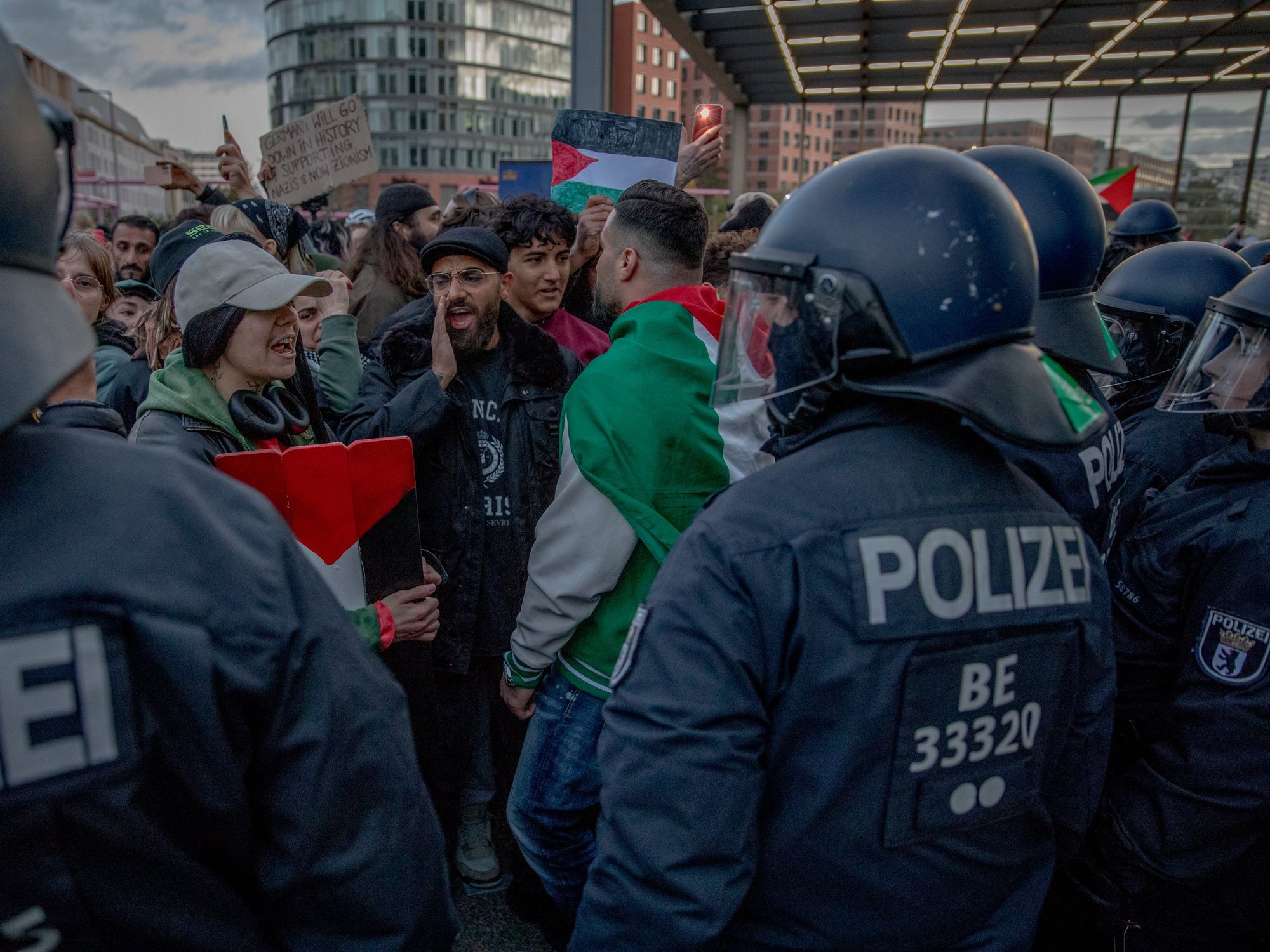 pro-Palestinian demonstrators stand in front of a line of policemen as they chant and wave flags.