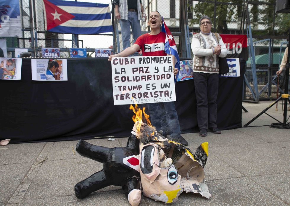 Protesters hold cuban flags and signs in the background as a papier maché figure of Donald Trump burns in the foreground