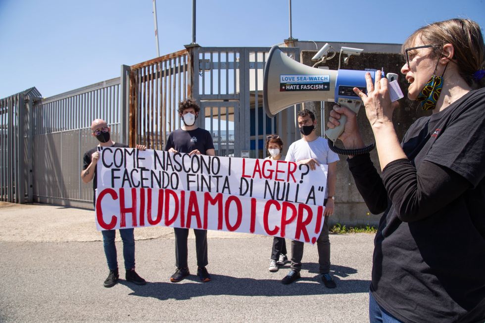 Protesters in medical masks hold up a sign while a woman speaks into a megaphone