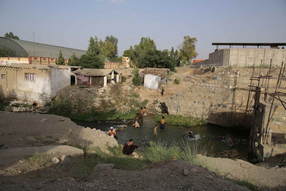 Residents living by Jalalabad airfield wash in the stream that flows from a hole in the high wall surrounding the base.