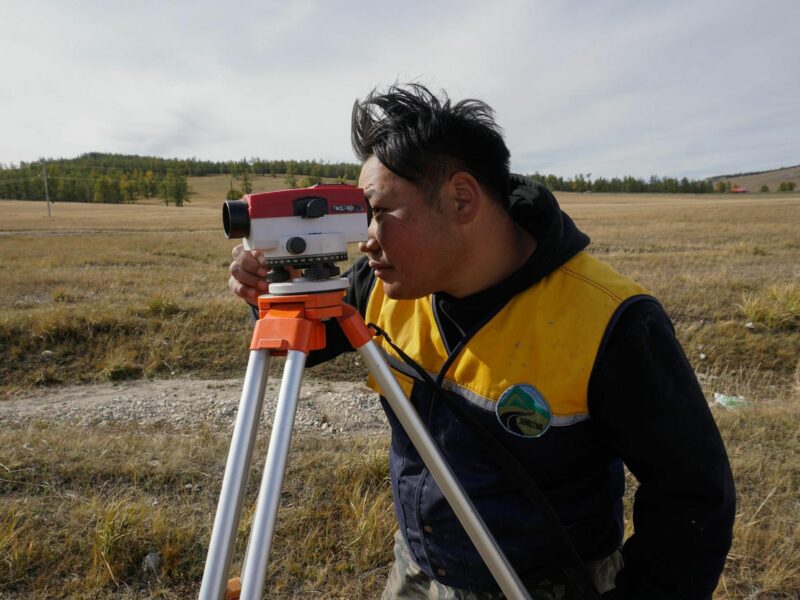 Road engineer looking through a scope on a metal tripod in the Mongolian steppe