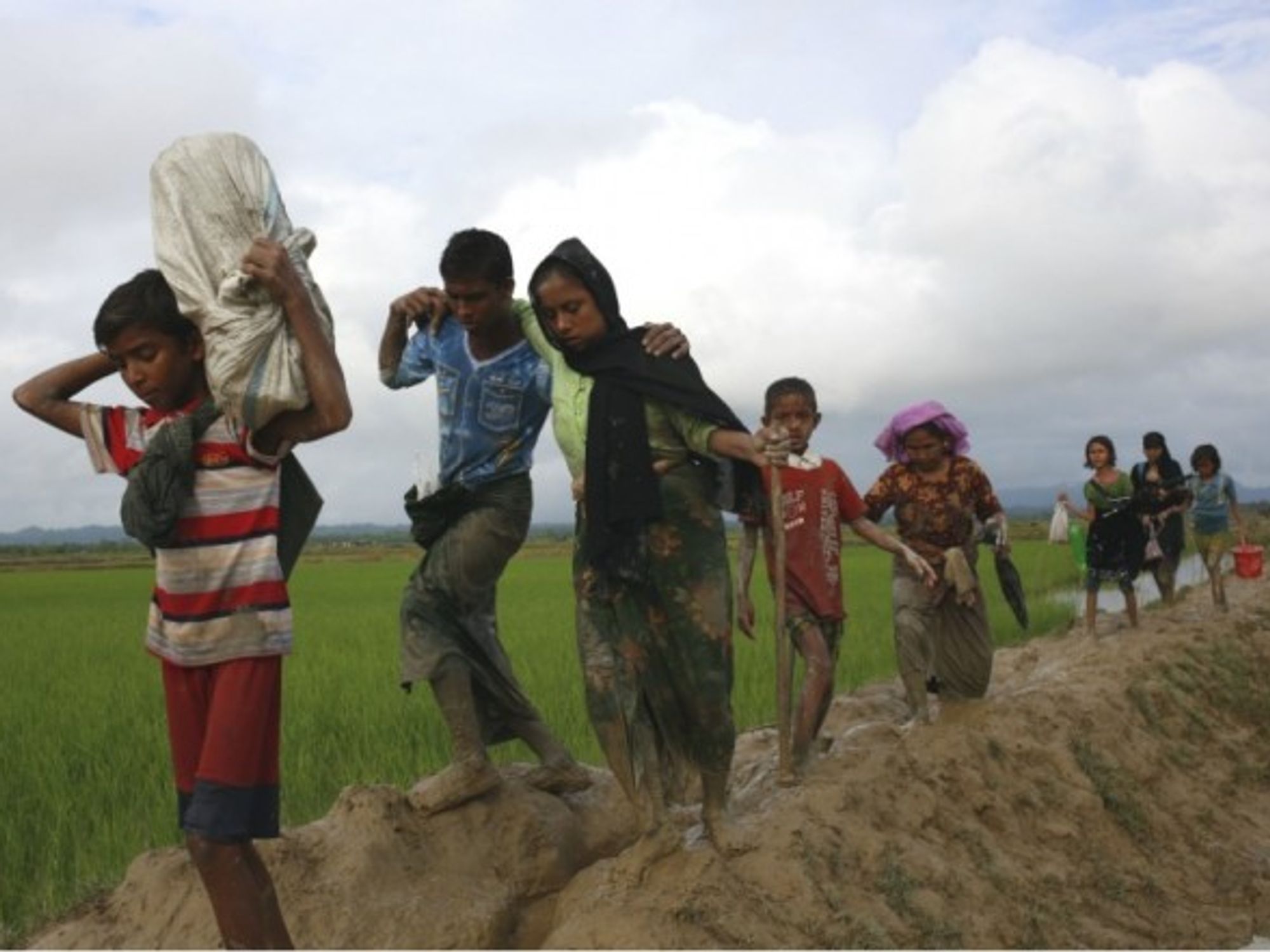 Rohingya refugees walk through the mud