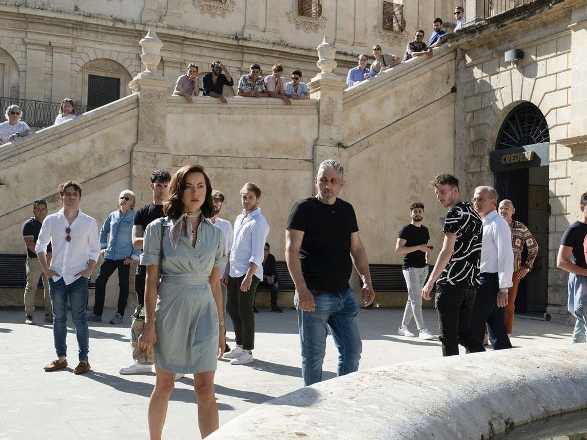 Screen-grab of The White Lotus, when Aubrey Plaza walks through a Sicilian piazza and men gather round to stare at her.