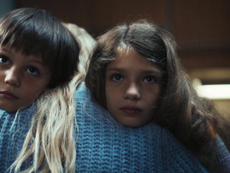 Screengrab from Netflix's Dear Child, showing two children, a boy and a girl, hugging a blonde woman.