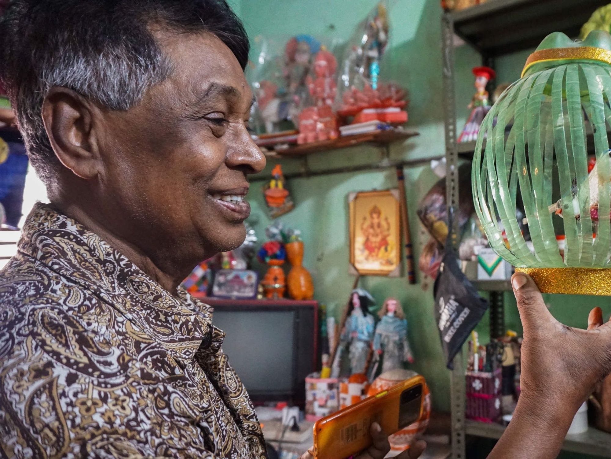 Shyamanand Singh holds up one of his creations, a bird in a cage made from discarded plastic and paper, at his home and art museum.