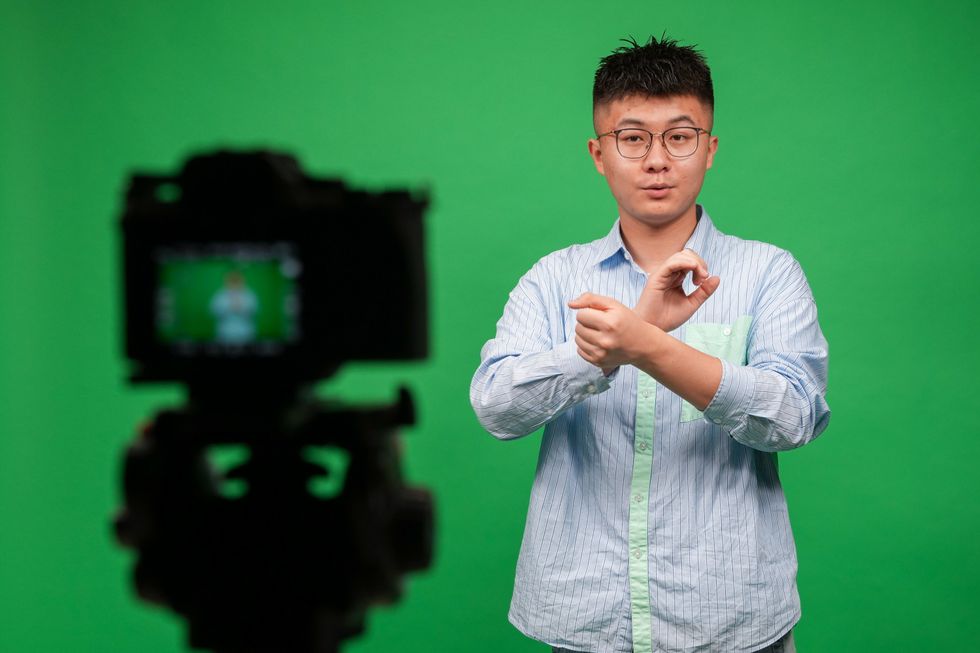 Sign language interpreter signs to camera infront of a green background