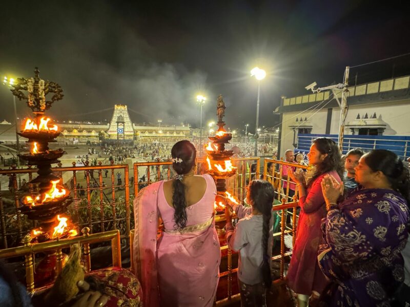 Small crowd gathers in front of an Indian temple at night lightning ceremonial torches.