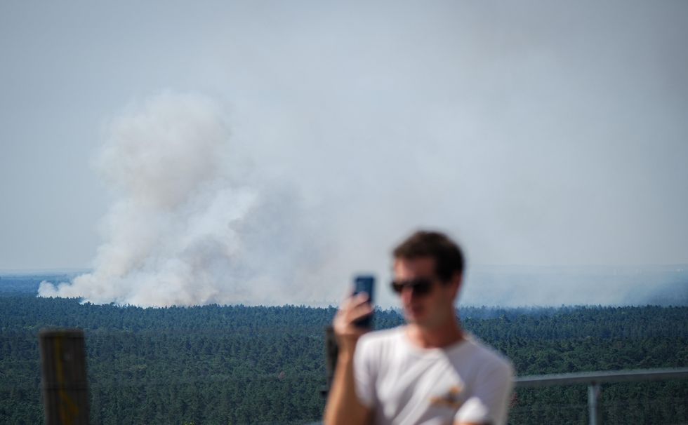Smoke rises behind a tourist during a fire in Grunewald, Germany