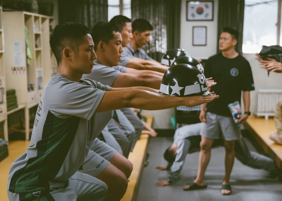 South Korean draftees squatting holding their helmet​ in Netflix's Korean drama D.P. (Deserter Pursuit)