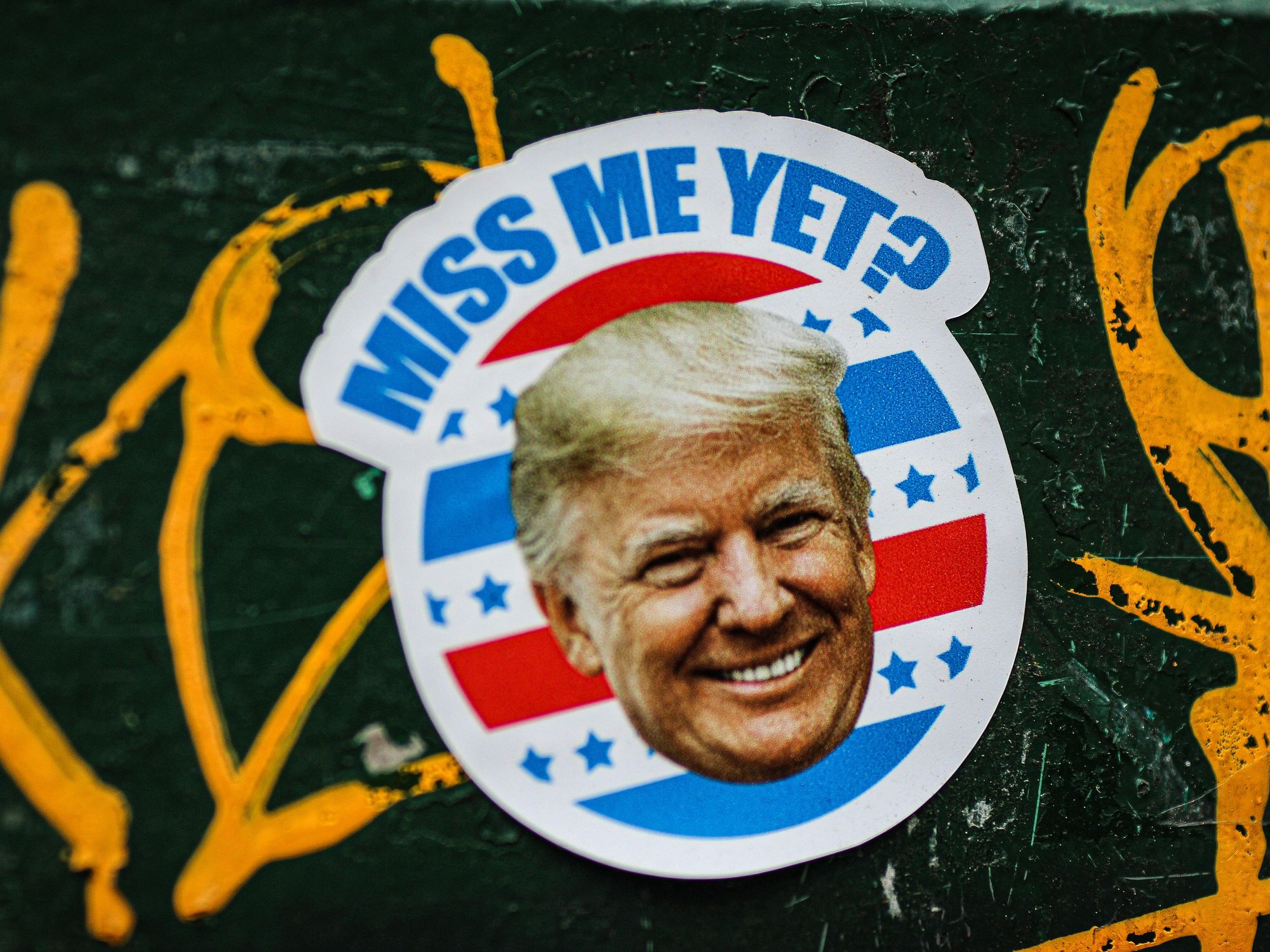 Sticker of Donald Trump on a wall that reads "miss me yet?"
