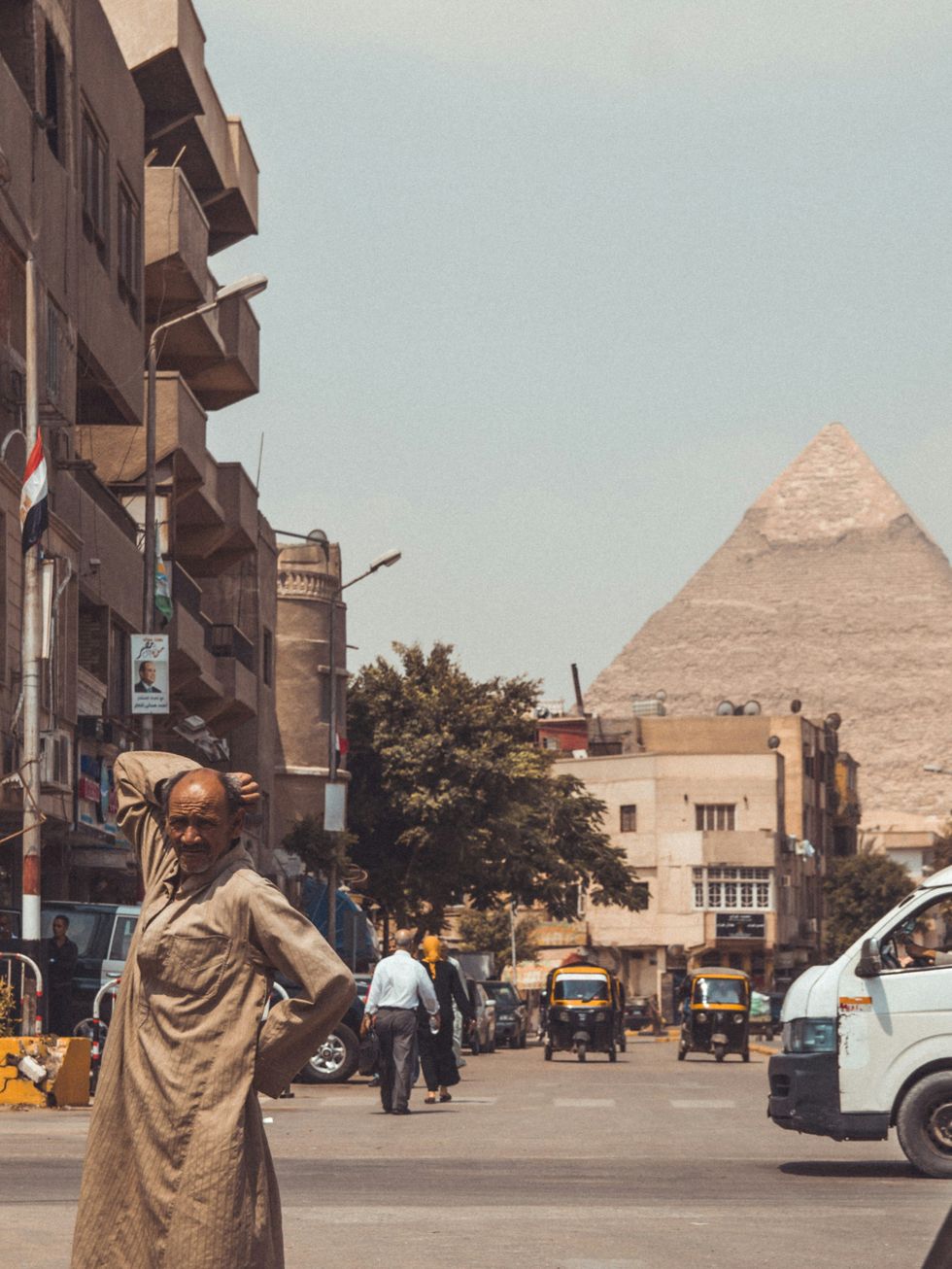 Street scene in Cairo with the Pyramids in the background and tuk-tuks navigating the streets