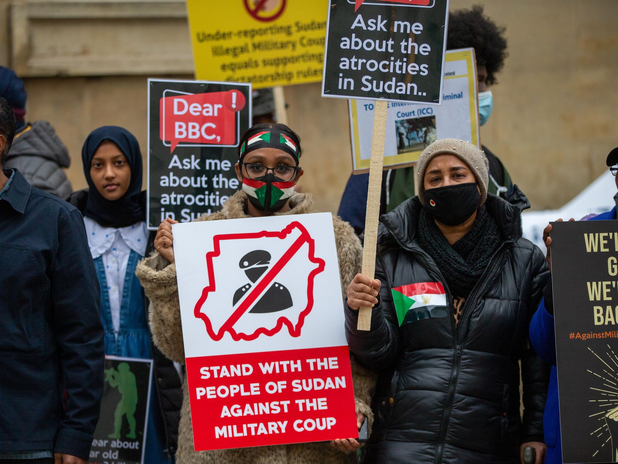 Sudanese protesters holding signs and wearing Sudanese flag