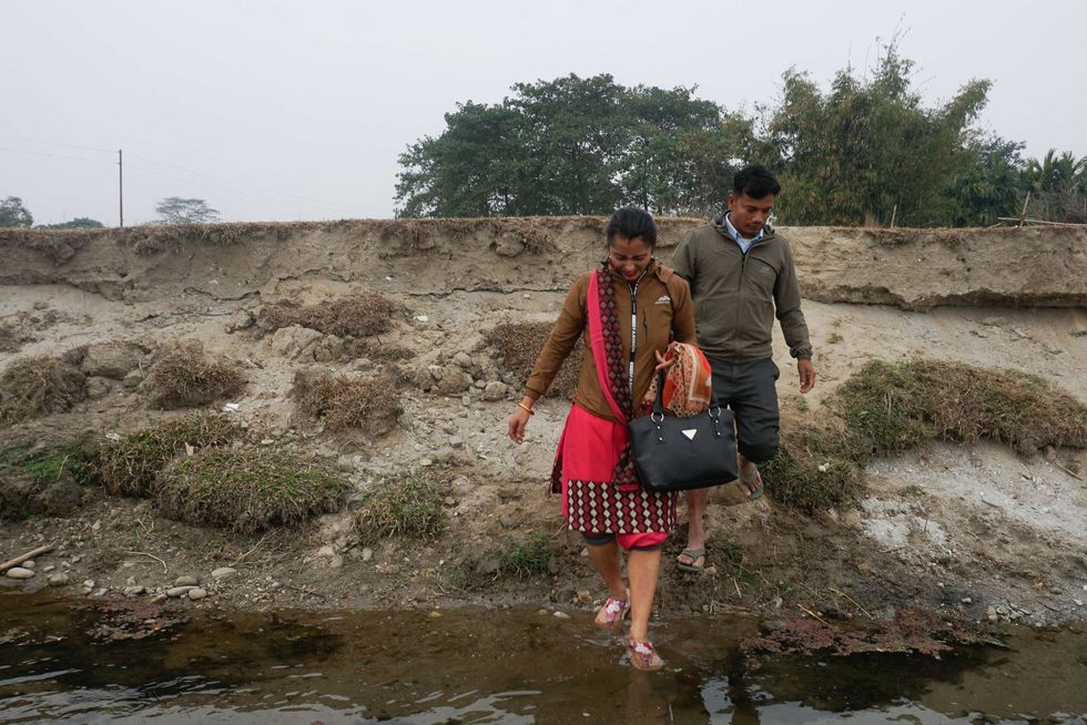 Teacher Rama Devi Dhakal, left, and office worker Rajesh Kumar Chaudary cross the river during their daily commute to Mechi Primary School in Gwalabasti hamlet, Mechinagar municipality.