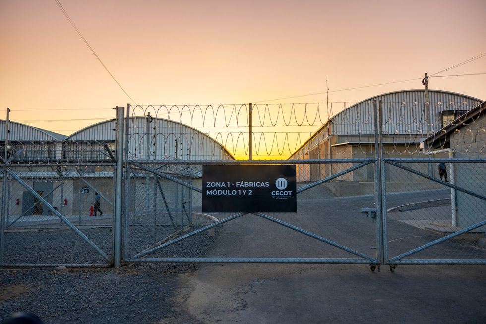 The front gate of the CECOT mega prison in El Salvador is illuminated from the sunrise behind it